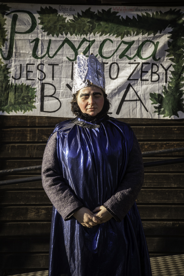 Król/Mędrzec (Julita Charytoniuk) pod budynkiem starej szkoły w Teremiskach na tle napisu Puszcza jest po to, żeby była.