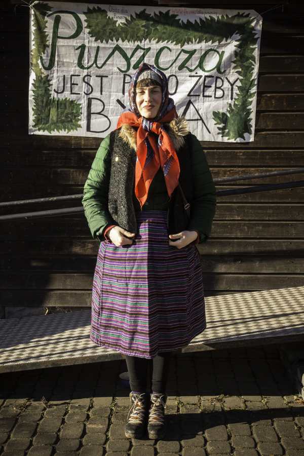 Baba (Agnieszka Zawadka) pod budynkiem starej szkoły w Teremiskach na tle napisu Puszcza jest po to, żeby była.